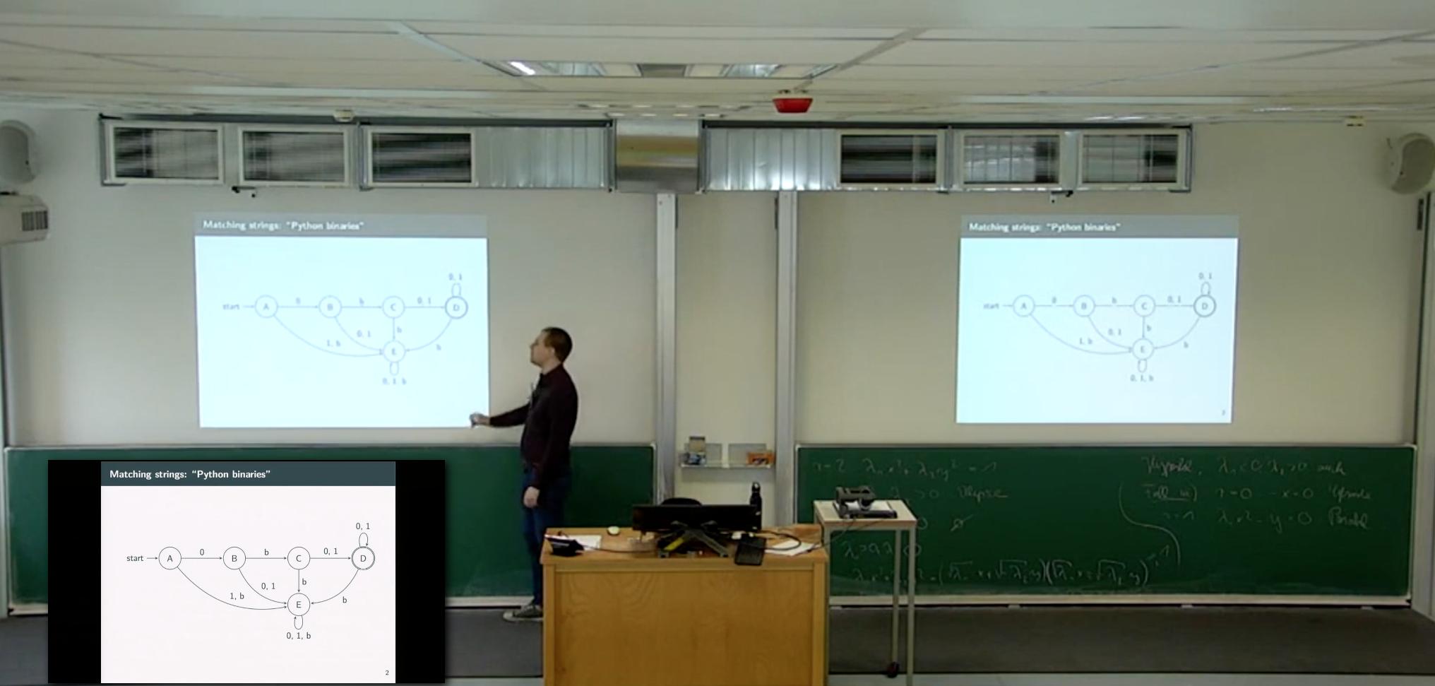 A still of a lecture recording. Sebastian Höffner is standing in frot of the beamer presentation and points to a slide showing a finite state automaton.